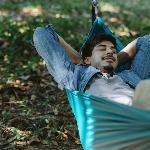 A man lounging back in a hammock, eyes closed, hands behind his head.