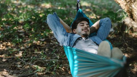 A man lounging back in a hammock, eyes closed, hands behind his head.