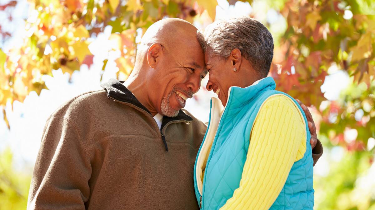 A couple standing close, foreheads pressed together, smiling at one another, under an autumn tree.