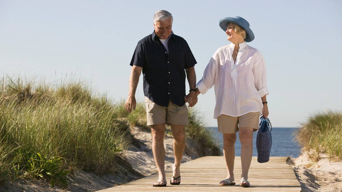 A couple walking hand in hand on a beach boardwalk, both smiling.