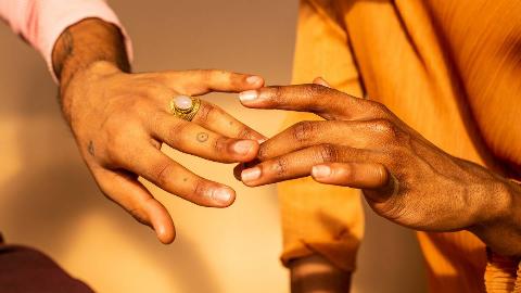 A close shot of two hands touching gingerly in the sun.