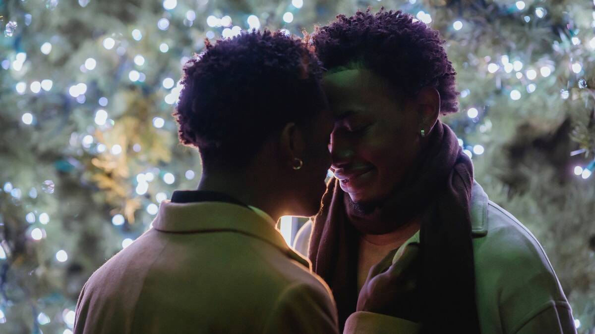  couple standing in front of some outdoor Christmas lights, their foreheads pressed together, eyes closed.