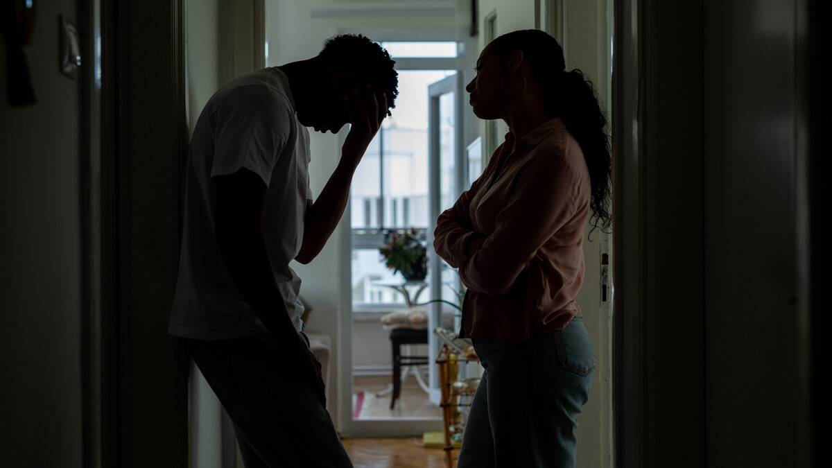 The silhouette of a couple standing in a doorway, the woman with her arms crossed, the man with his forehead in his hand.