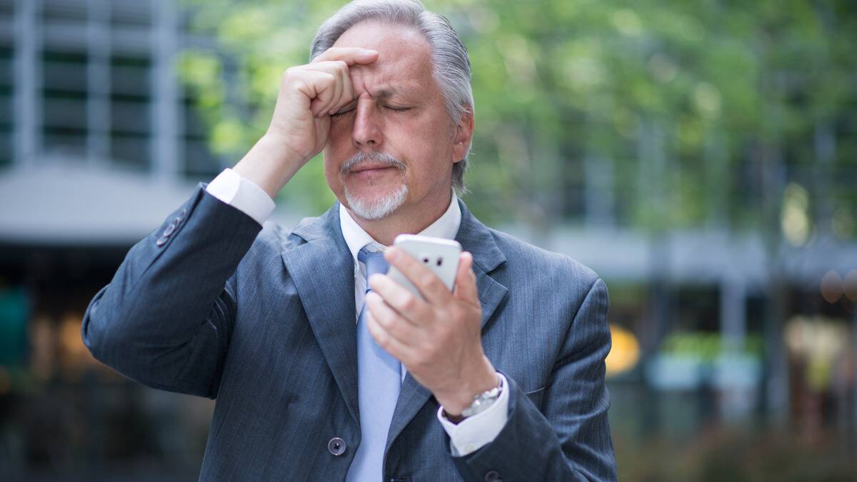 A man holding his phone, eyebrows furrowed, eyes closed, a hand on his forehead, clearly having forgotten something.