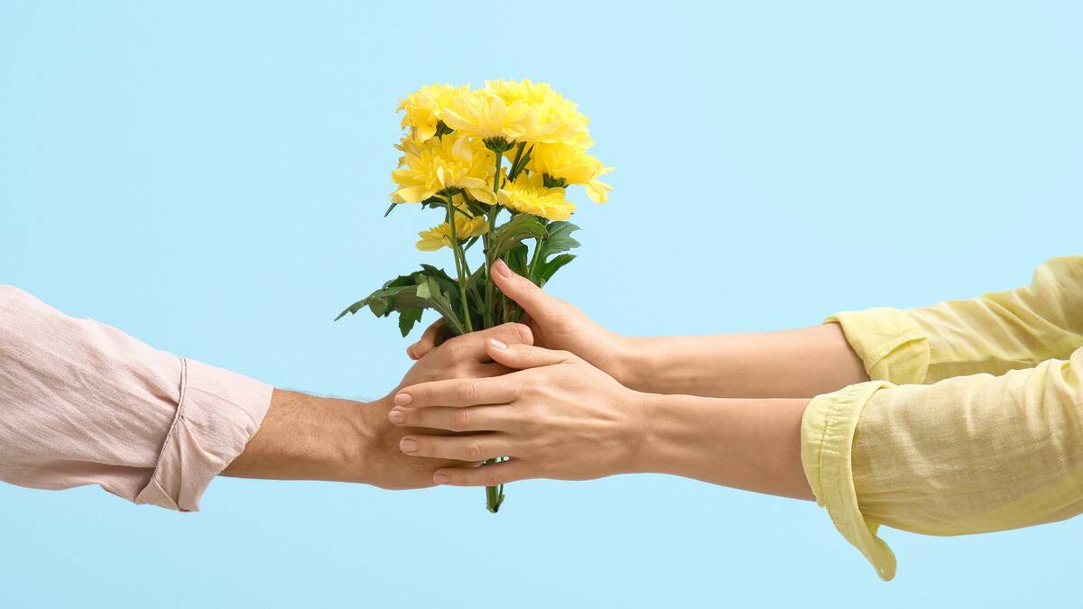 Someone handing a bouquet of yellow flowers to someone else, who's taking it with two hands.