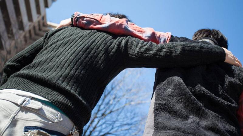 A low-angle shot of two people standing side by side with an arm around each other's shoulder.