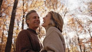 A low angle shot of a couple standing close outside, both smiling and laughing.