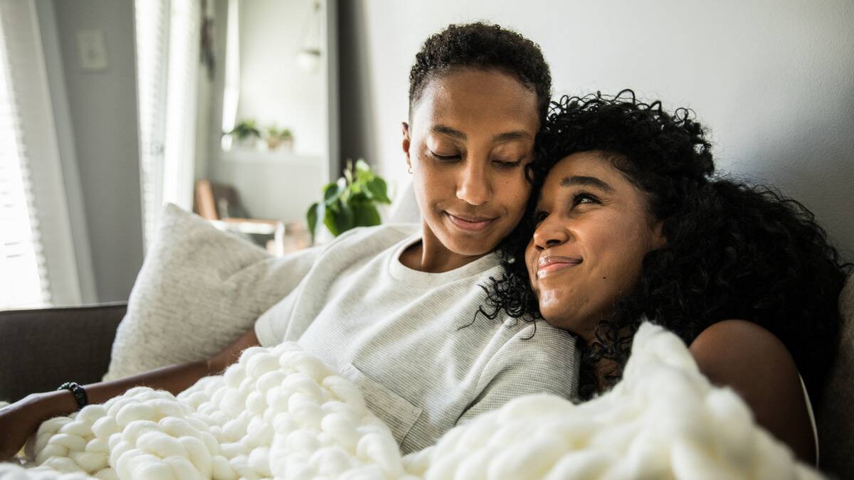 A couple cuddled up on the couch together, smiling at each other.