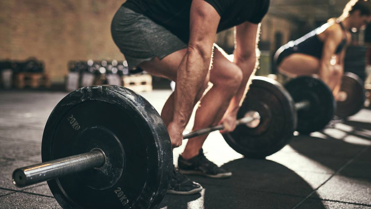 Someone bent down and grabbing a barbell with large plates on it, about to deadlift.