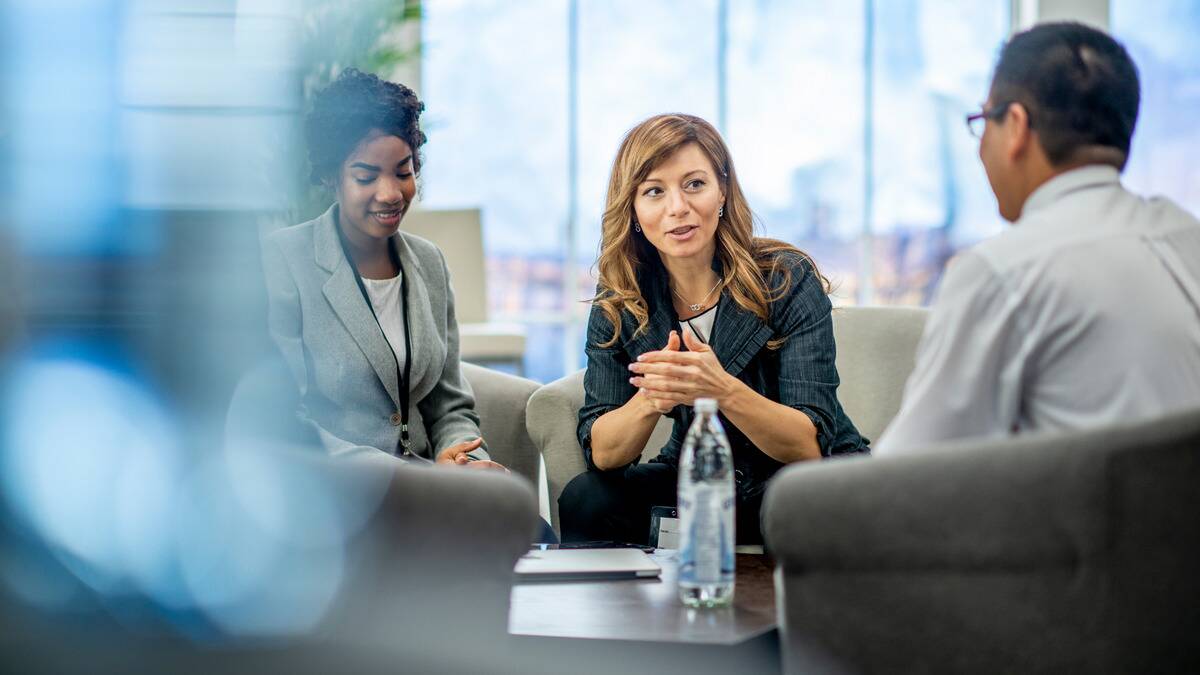 A woman sitting with some of her colleagues, speaking confidently about something.