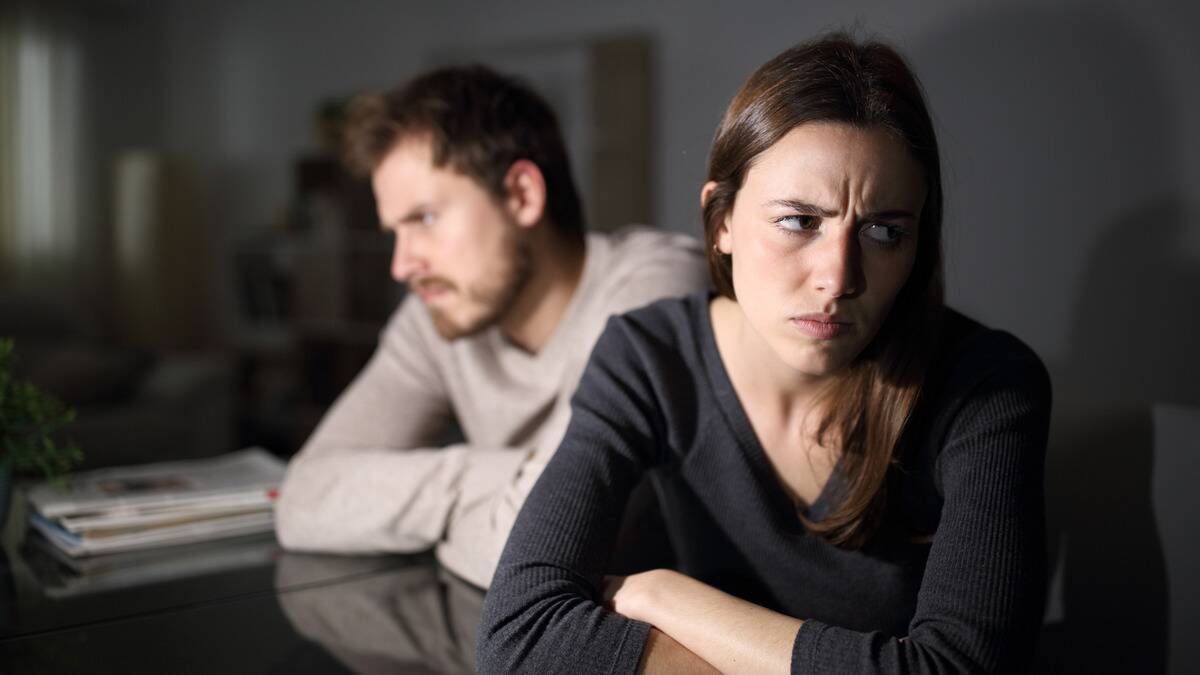 A woman with her arms crossed sporting an annoyed expression facing away from a man who's sitting behind her, also with his arms crossed looking annoyed.