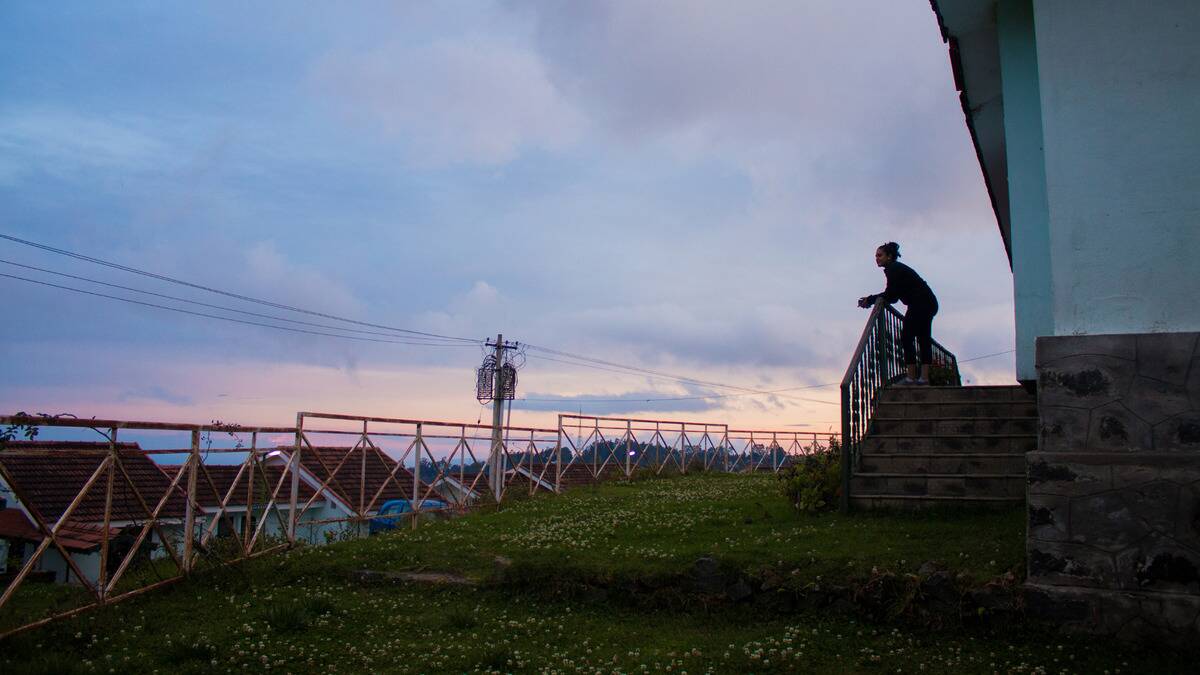 Someone standing on the front port of their home, leaning on the railing, looking toward the horizon.