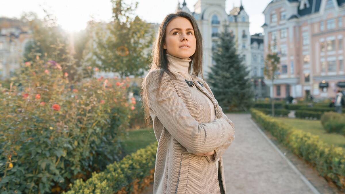 A woman standing in a courtyard with her arms folded, looking off into the distance.