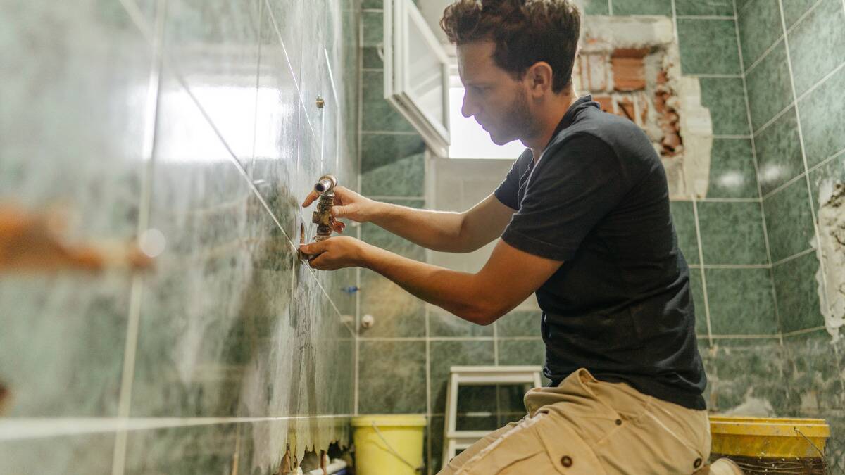 A man knelt on the ground as he renovates his bathroom, replacing the faucet.