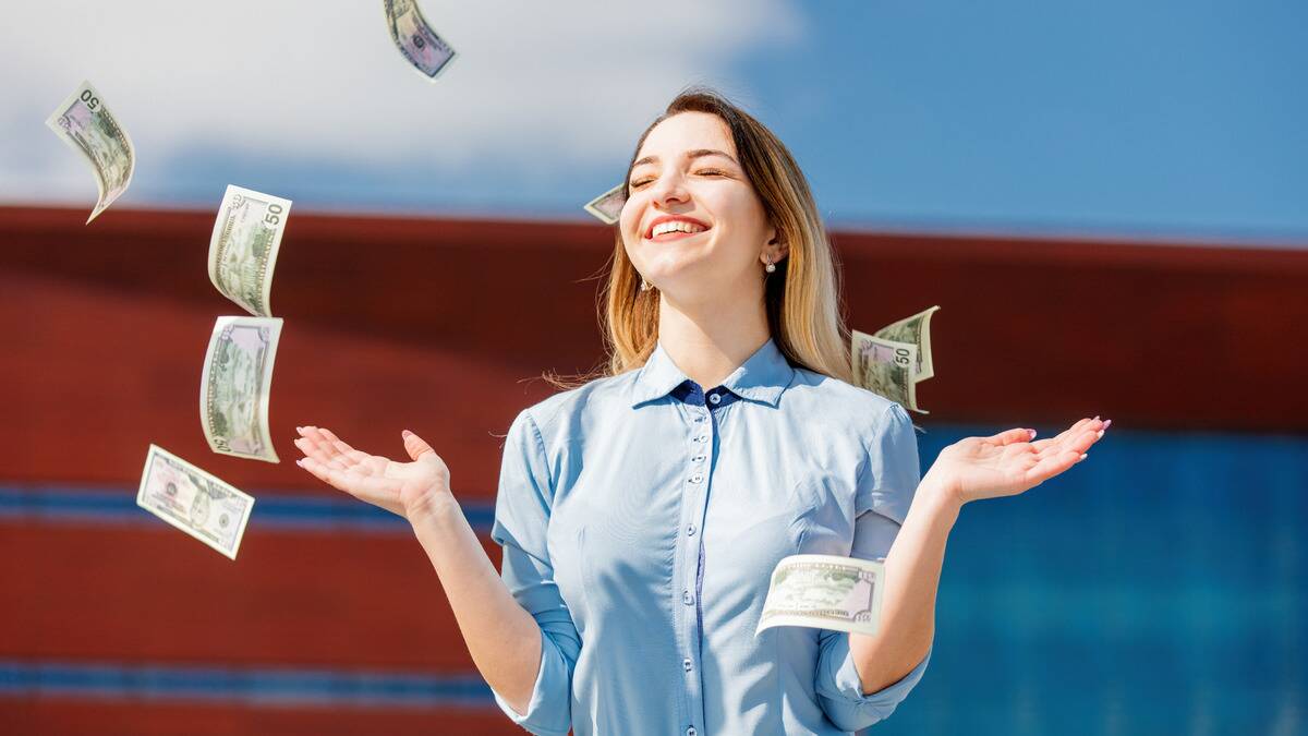 A woman smiling with her hands out as American $50 bills fall around her.