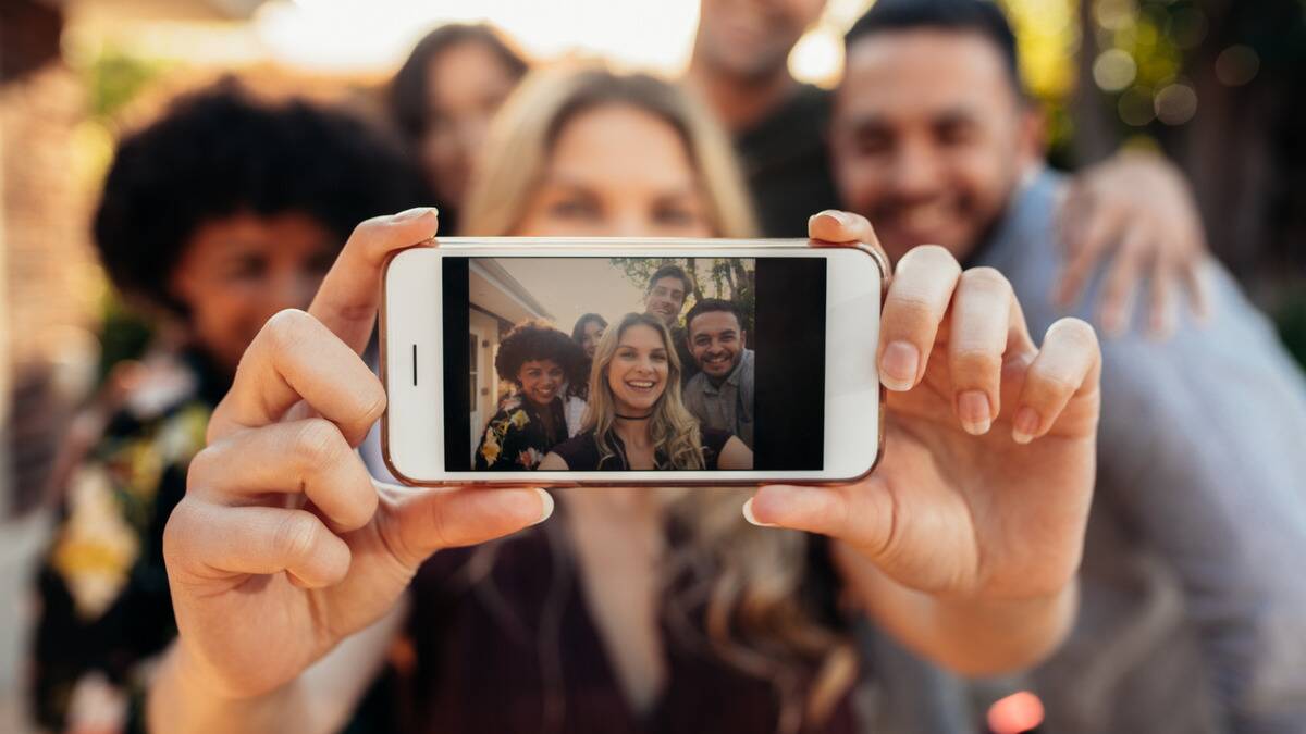 A group of friends as seen through a phone screen as one of them takes a selfie.