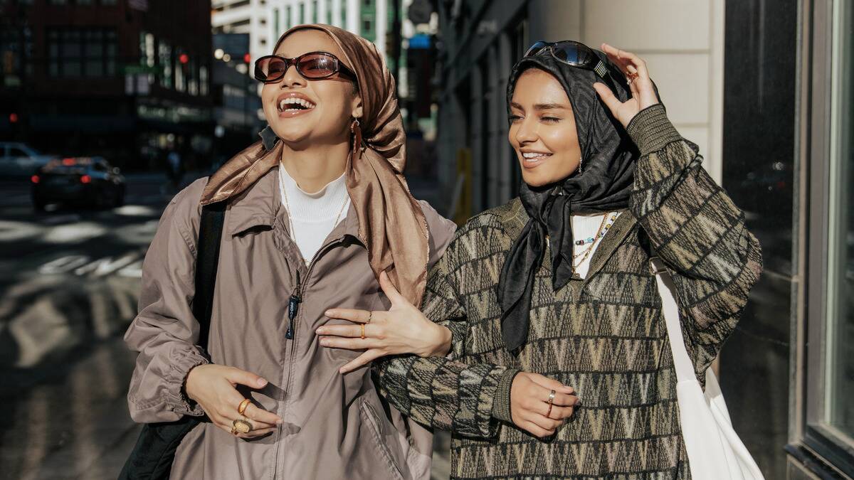 Two stylish young women waling down the street, arms linked while they smile.