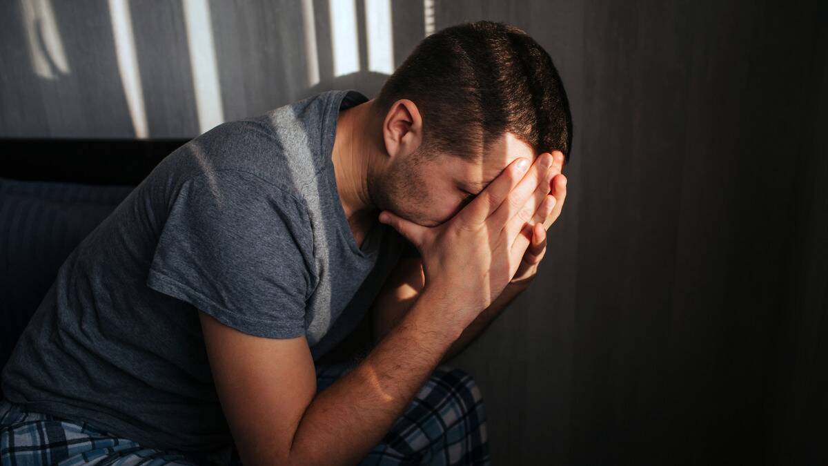 A man sitting inside, leaning forward with his elbows on his knees, face in his hands.