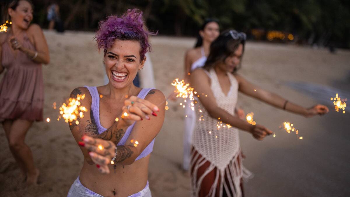 A group of friends having fun on the beach at dusk, all dancing with sparklers.