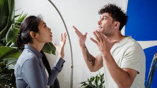 A couple in the midst of arguing, both looking stressed and gesturing dramatically with their hands.