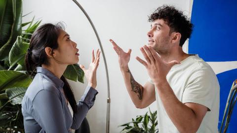 A couple in the midst of arguing, both looking stressed and gesturing dramatically with their hands.