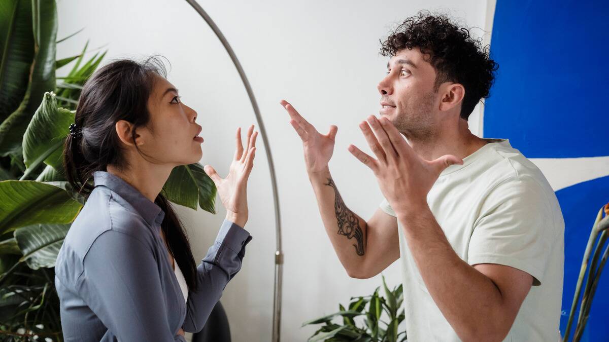 A couple in the midst of arguing, both looking stressed and gesturing dramatically with their hands.