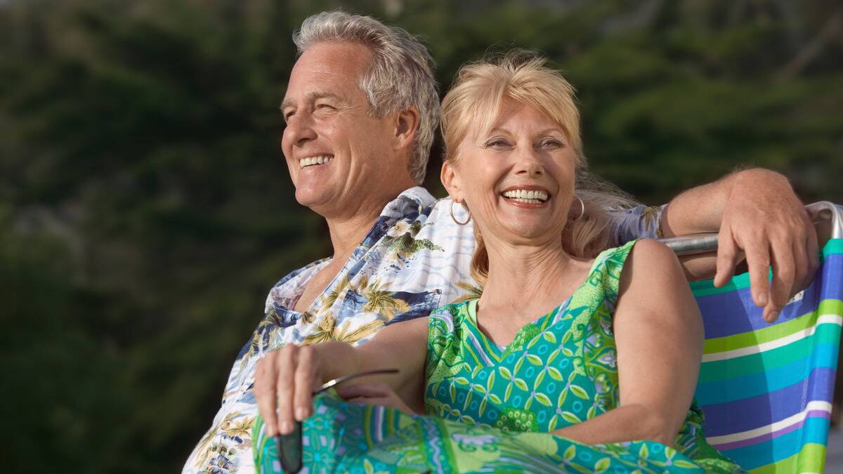 A couple sitting outside in the sunshine, smiling brightly, in summer wear.