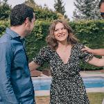 A woman standing with her two male friends, an arm out to each of them, all smiling as they chat.