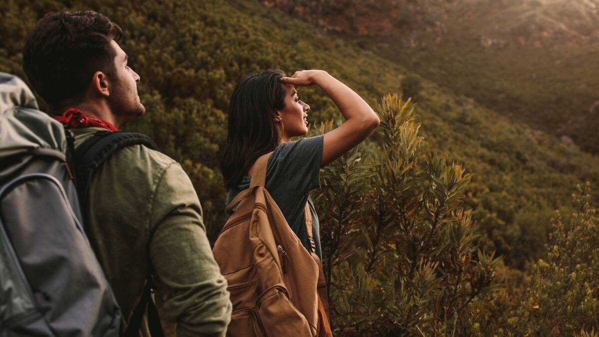 A man and woman out hiking together, the woman one step ahead, a hand to her brow to block out the sun as she looks forward.