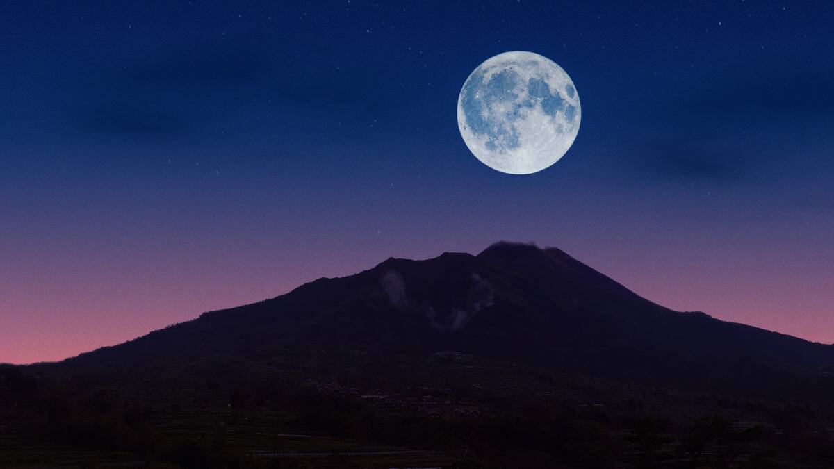 The full moon risen over the tip of a mountain.