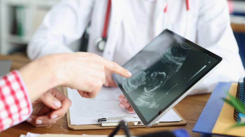 A close shot of a pair of hands pointing at an ultrasound being shown on a tablet held by a doctor.