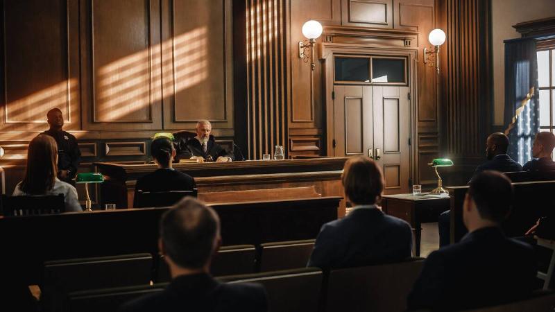 A photo of a courtroom, a judge behind the stand and people in attendance.