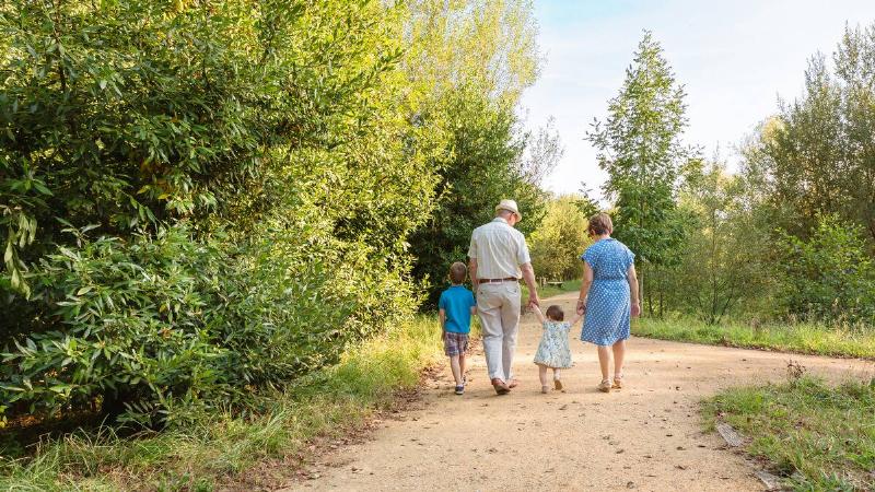 Two grandparents walking with their two young grandchildren down a dirt walking path.