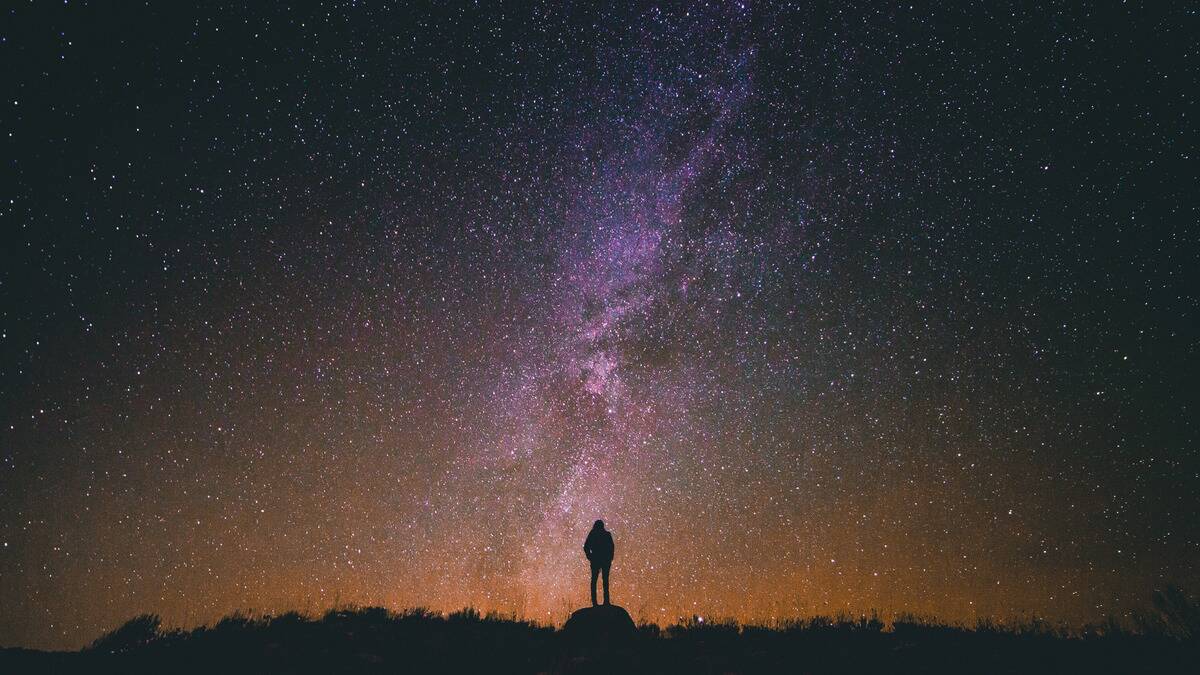 The silhouette of a person standing below a mystical, beautiful expanse of sky filled with stars.