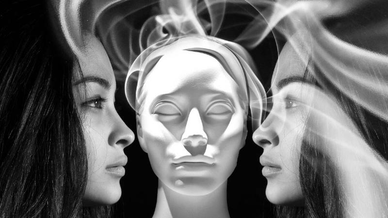 In the center is a mannequin head, on either side is a woman's face in profile, smoke swirling all around them.