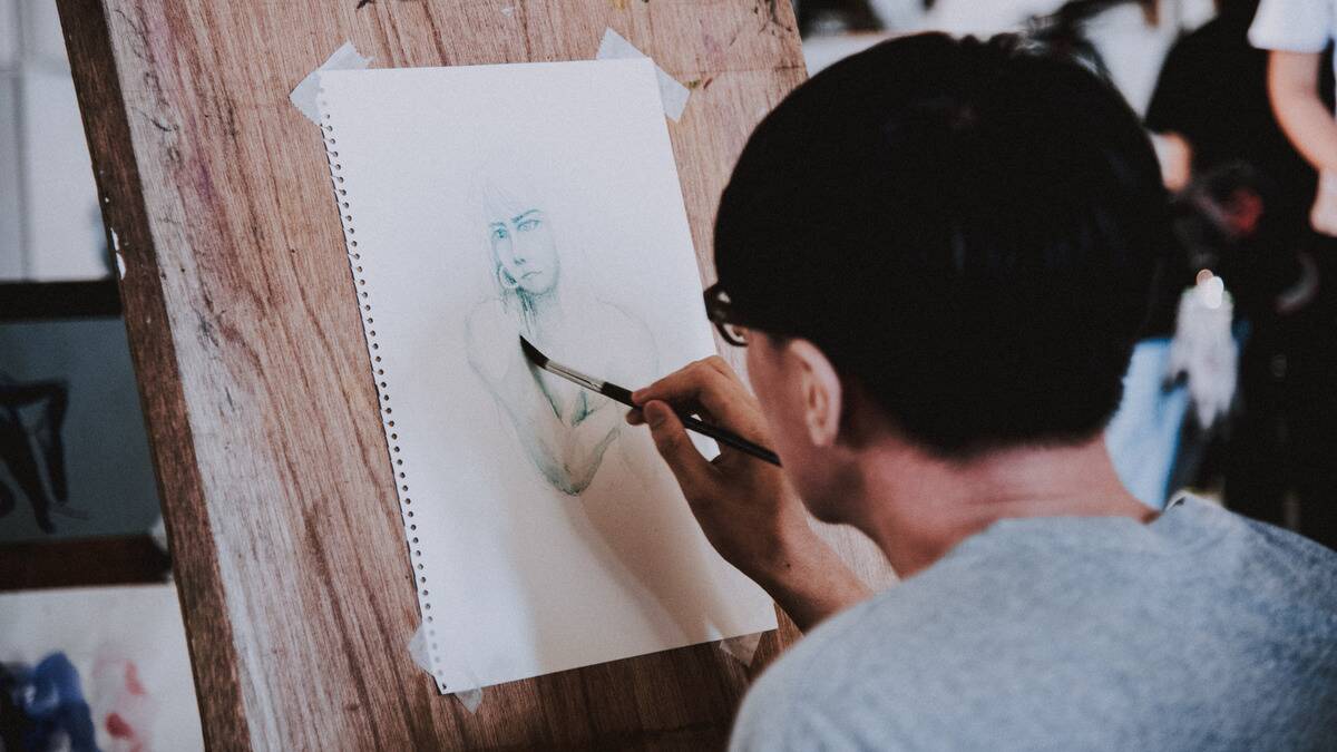 An over-the-shoulder shot of a man painting a portrait.