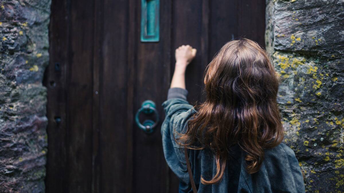 A woman knocking on a large, old door.