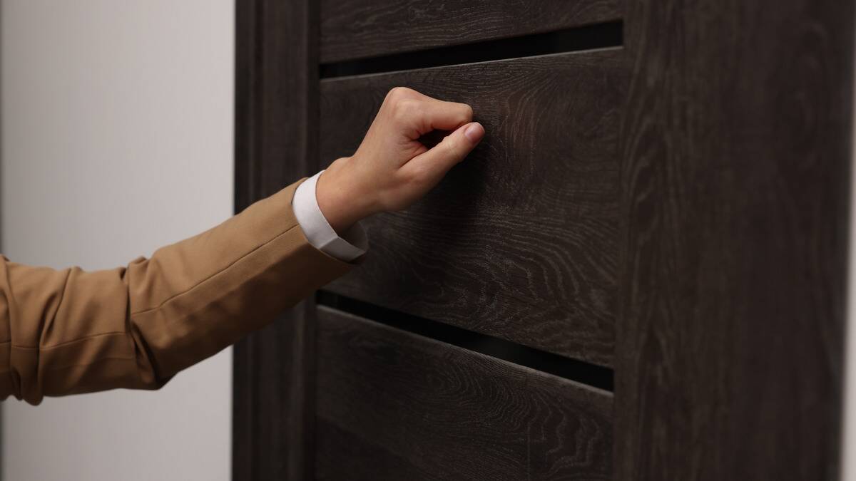 A hand knocking on a dark wood door.