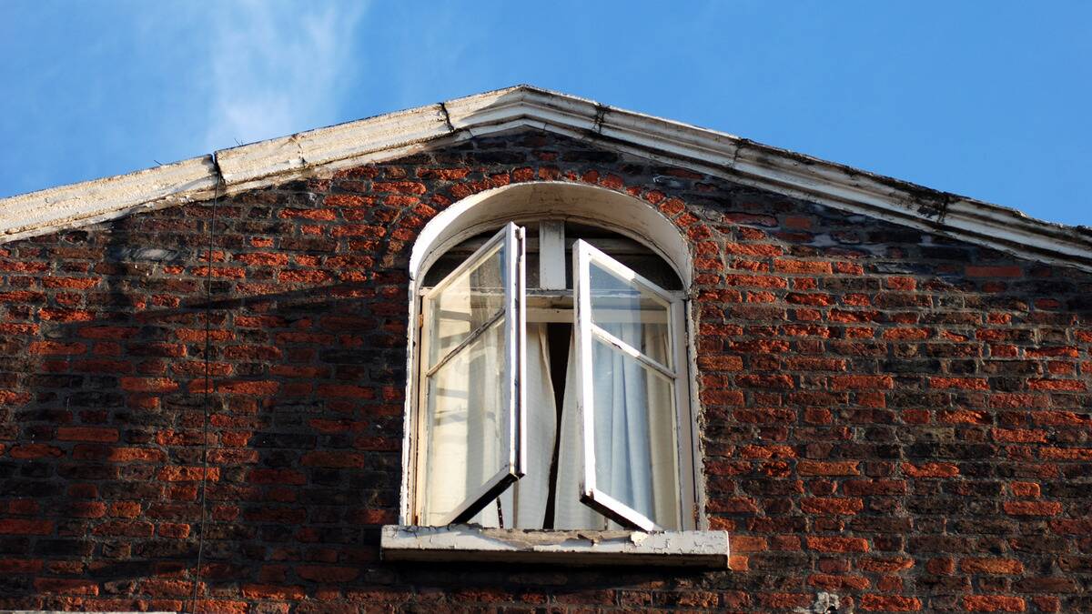 A photo of an arched window on the top floor of an old out, photographed from outside.