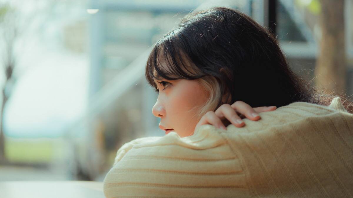 A close, profile shot of a woman leaning her chin against her folded arms, looking up at the world in front of her.