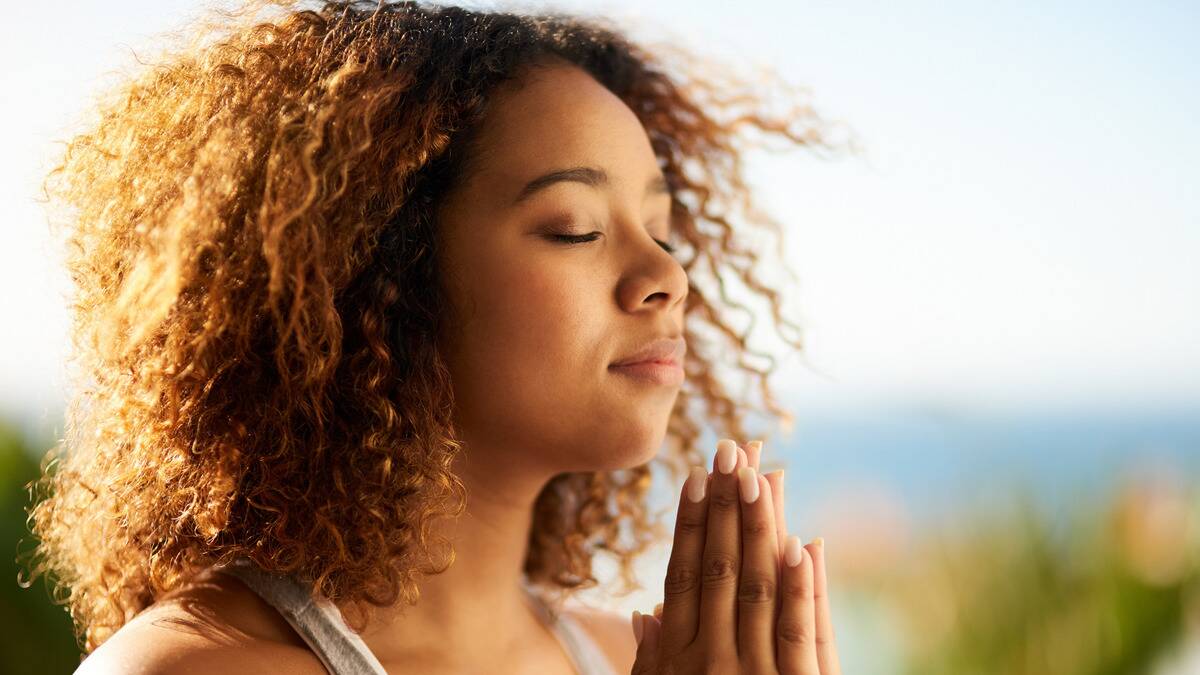 A woman with her eyes closed and hands pressed together in prayer.