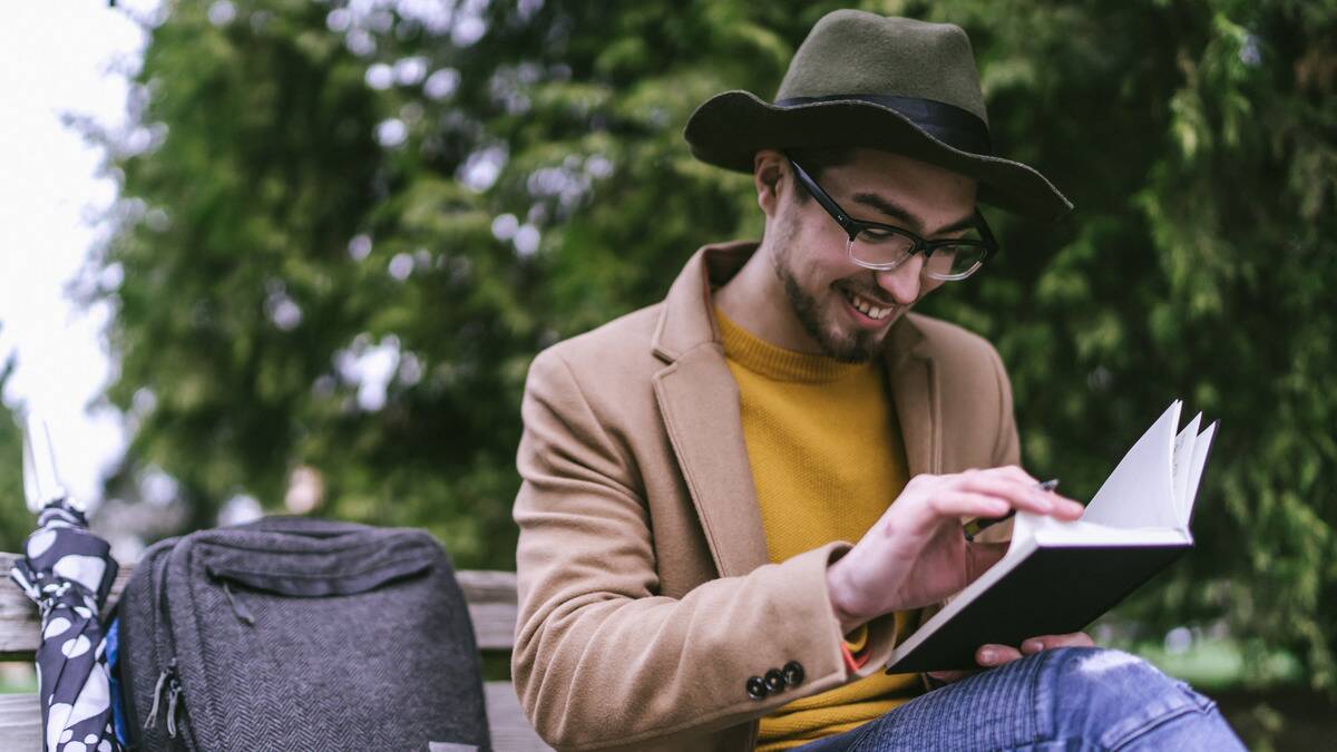 A man sitting on a bench outside, smiling as he flips through his journal.