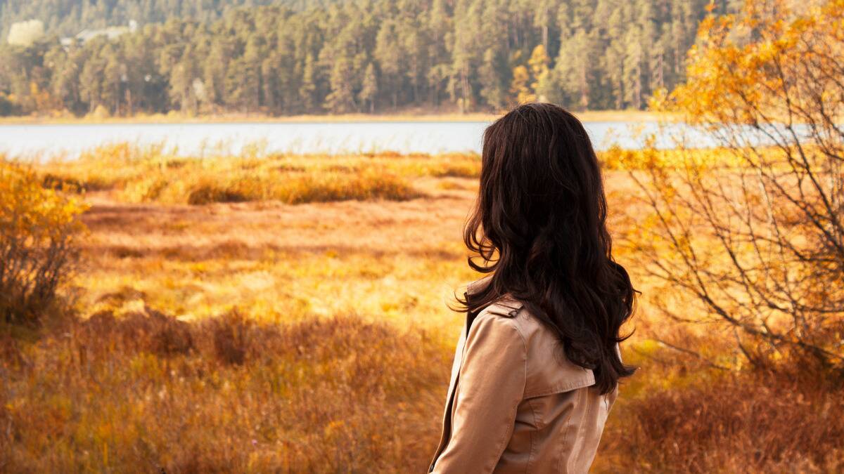 A woman looking forward, away from the camera, toward the field and river she's standing beside.