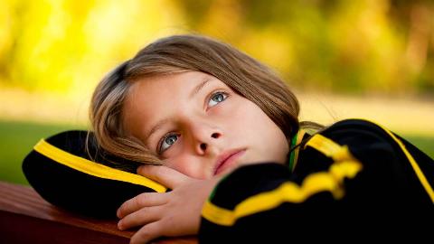 A child with their head resting on their folded arms looking up toward the sky forlornly.