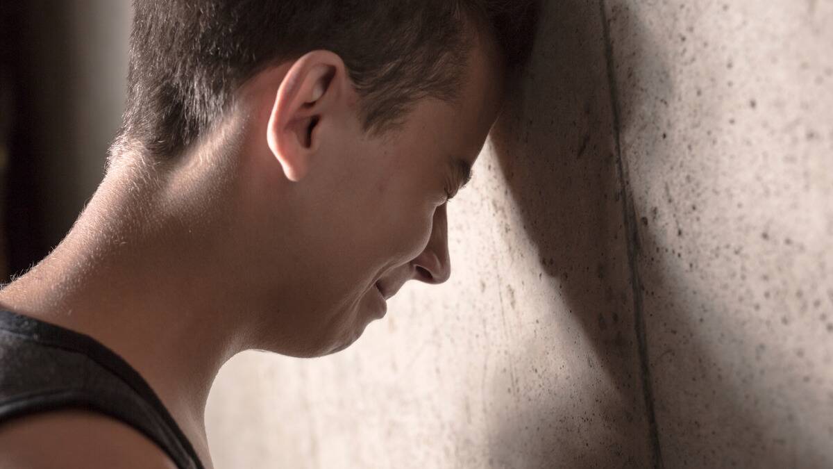 A close shot of a man who's pressing his forehead into the wall as he cries, face tight.