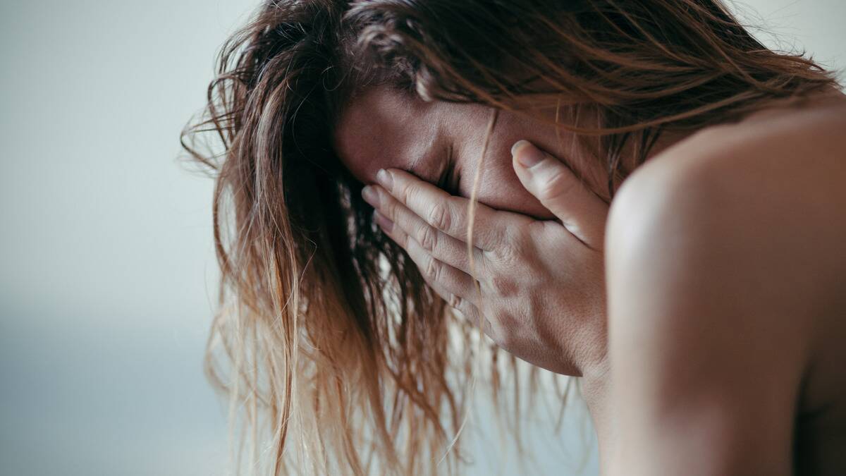 A close shot of a woman with her head leaning foward, covering her face with her hands, looking distressed.