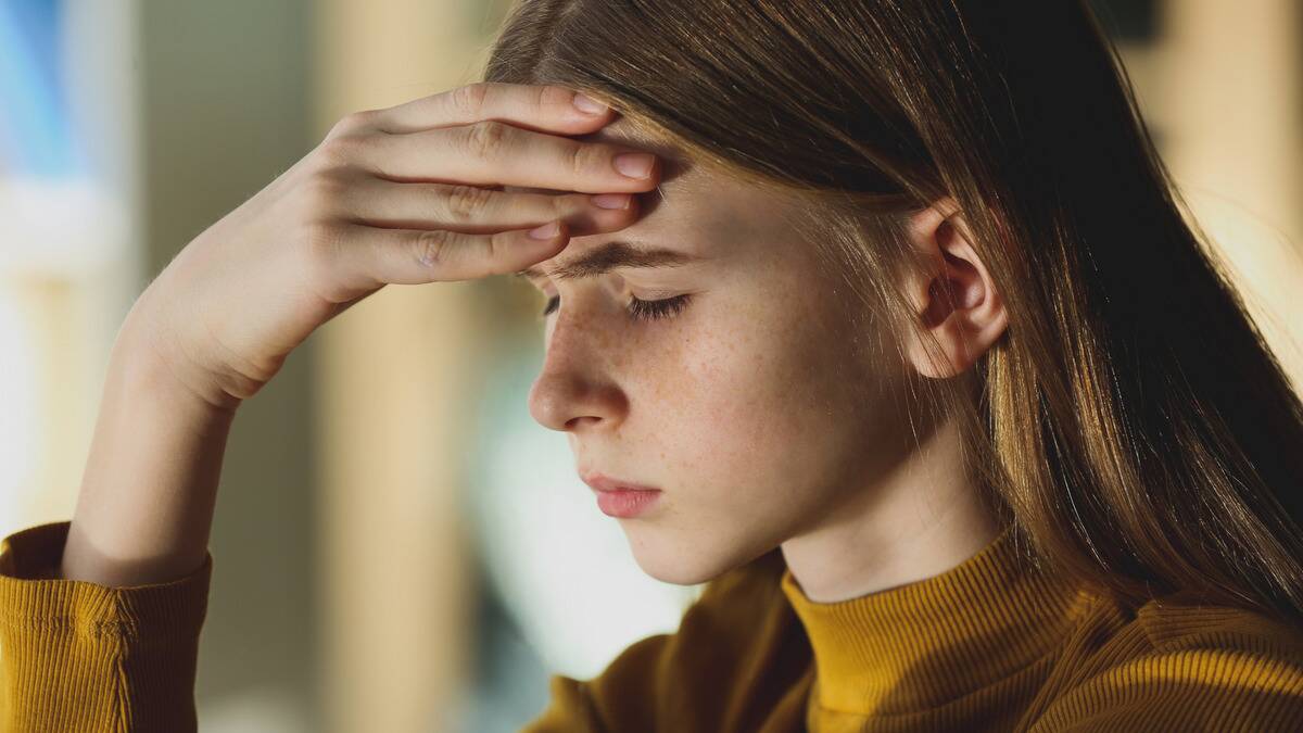 A young girl with a hand on her forehead, eyes closed, looking frustrated.