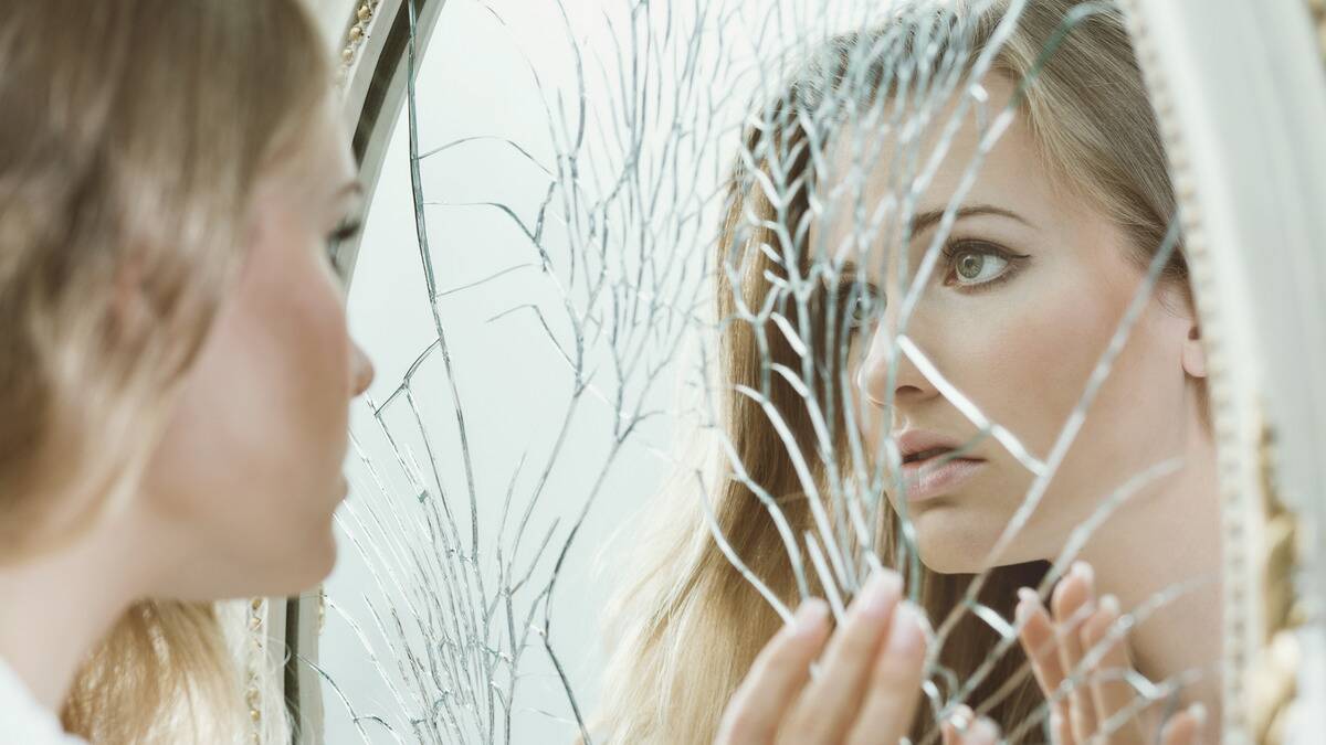 A woman staring at herself in a shattered mirror.