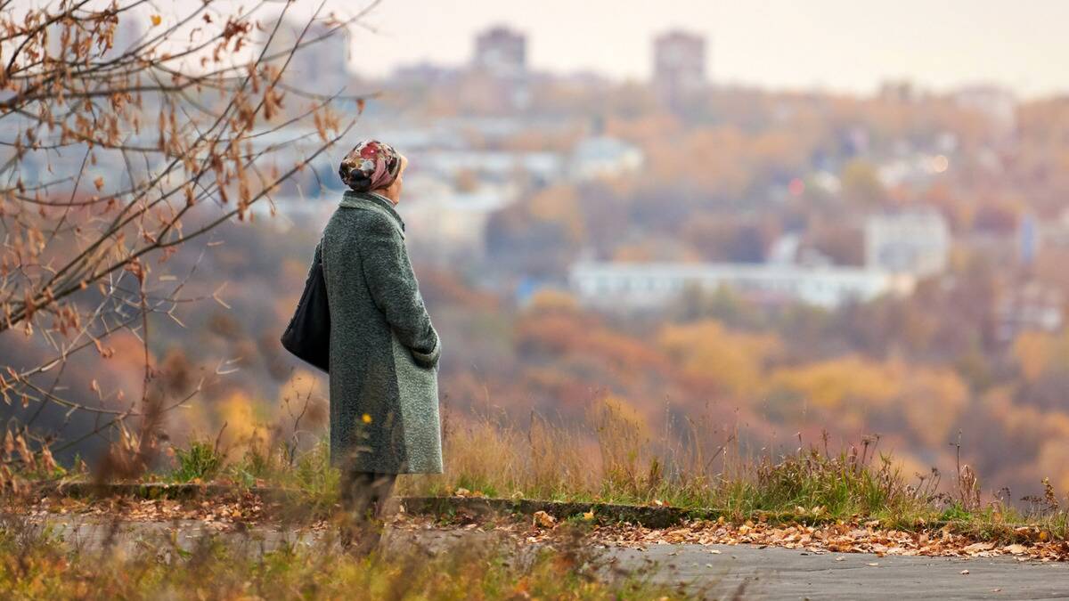 A woman standing on a path during fall, overlooking the city and trees around it.