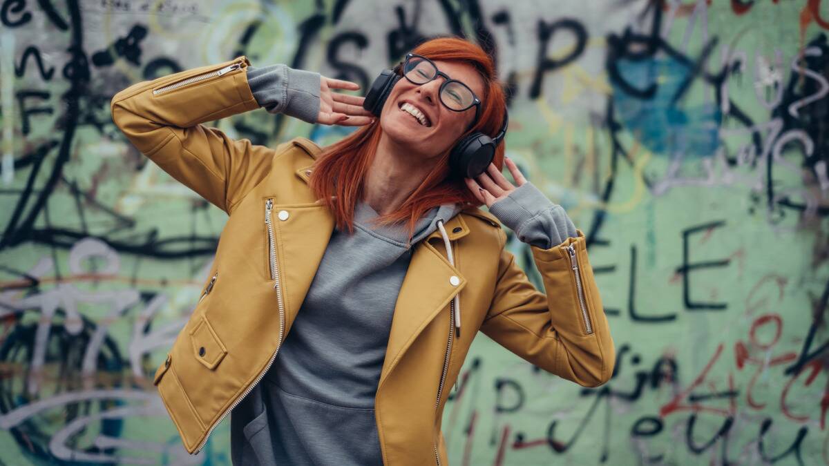 A woman outside dancing with headphones on, smiling brightly.